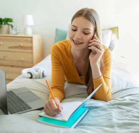 Girl Working From Home on Bed With Laptop and Notebook